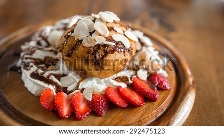 Close up fried ice cream with almond, whipped cream and strawberry on wood dish
