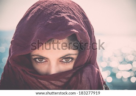 mysterious woman with her face covered and only her eyes showing with a vintage filter applied