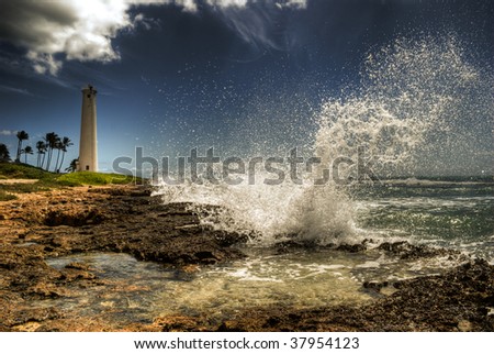 HDR wave crashing into rocky shore, Barber\'s Point Lighthouse in background, taken on Oahu, Hawaii.
