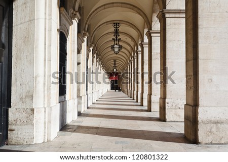 Sunlight and shadows in long marble covered corridor with ornate wrought iron lamps hanging from vaulted ceiling in the buildings surrounding the Praca Del Comercio Lisbon Portugal