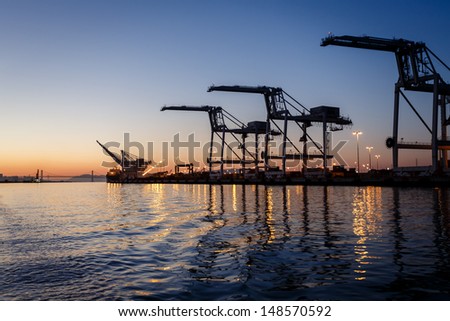 Alameda, California gantry cranes loom high above water at sunset in San Francisco Bay waiting for ships to fill