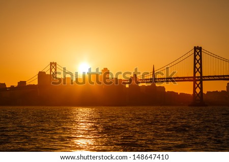 Brilliant golden glow back lights San Francisco skyline and and reflects on the water under the Bay Bridge