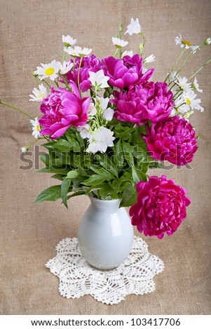 Bouquet of peonies and daisies in a white vase on a lace napkin