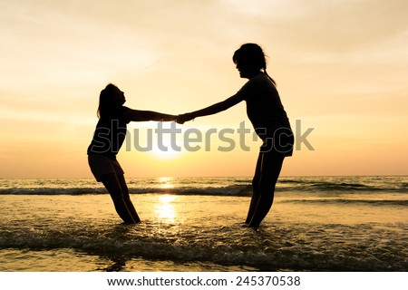 Silhouette of two women hold hand in sunset sky at the sea. Happiness concept.