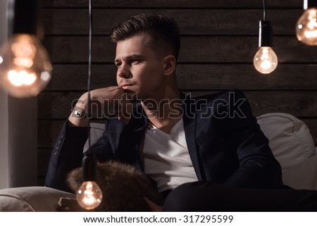 Thoughtful Handsome Man In Suit Sitting On Sofa Between Lamp On Wooden background