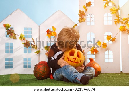Little Boy Holding Halloween Pumpkin Near Little Houses On Blue Background