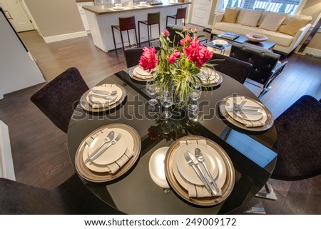Modern round dining room table set for dinner in a luxury  house, with a kitchen in the background. Interior design.