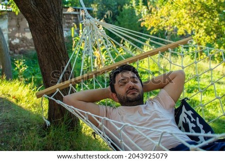 A man is resting in a hammock in a country house. A young guy lies in a hammock, dozing outdoors in the summer in the green of trees in the country. Stok fotoğraf © 
