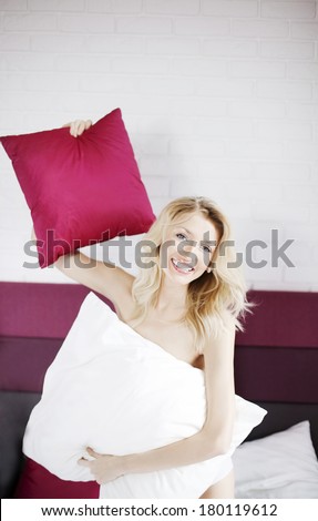 Smiling happy blonde young woman playing in bed at morning, looking at camera.