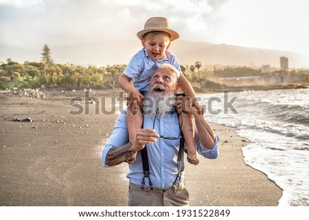 Happy kid playing on the beach with his grandfather, celebrating grandfather's day together, smiling, having fun. Real people emotions and family lifestyle concept. Summer time. Stock fotó © 