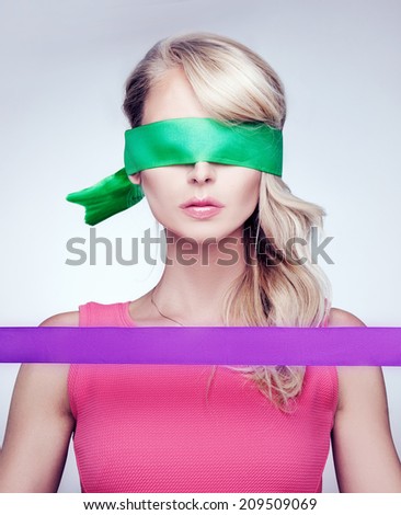 Portrait of woman with eyes covered with silk green ribbon, holding other purple. Conceptual photo. Attractive blonde girl.