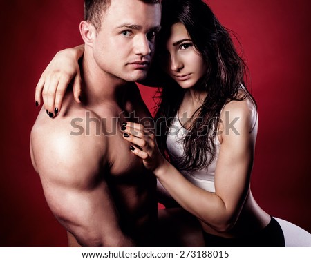 Portrait of handsome athletic couple over red background. Man and woman hugging.