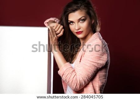 Young beautiful brunette woman showing empty white board, posing in studio. Girl looking at camera.