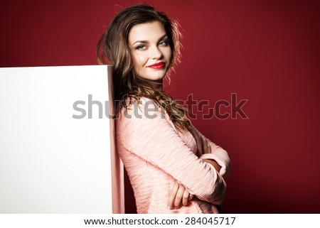 Young beautiful brunette woman posing with empty white board, posing in studio. Girl looking at camera and smiling.