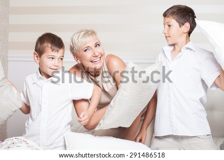 Family pillow fight. Smiling mother having fun with two little sons. Indoor photo.