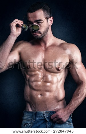 Handsome muscular young man posing shirtless with sunglasses.