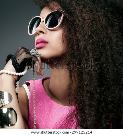 Fashion photo of beautiful elegant african american woman. Girl posing with a lot of jewelry, wearing fashionable sunglasses. Girl with long curly healthy hair. Beauty portrait. Studio shot.