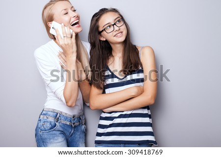 Two beautiful sisters posing together. Blonde girl talking by mobile phone. Studio shot. Lifestyle.