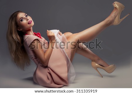 Fashionable young beautiful woman posing in studio, wearing pink dress and high heels. Girl with long slim legs.