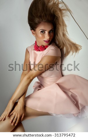 Fashionable young beautiful woman posing in studio, wearing pink dress. Girl with long slim legs.