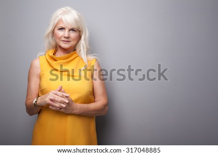Portrait of beautiful fashionable senior woman with long grey hair. Lady wearing yellow dress, looking at camera. Studio shot.