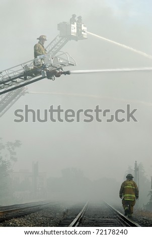DAYTON, OHIO - AUGUST 15: Firefighters battle a warehouse fire from aerial ladders as a lone fireman walks the track through a haze of smoke and water mist on August 15, 2008 in Dayton, Ohio, USA.