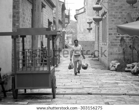 Wuhan, China - July 2, 2014.  This photo is taken in Wuhan, China and is of a Chinese man carrying two bags down a street. Black and white.