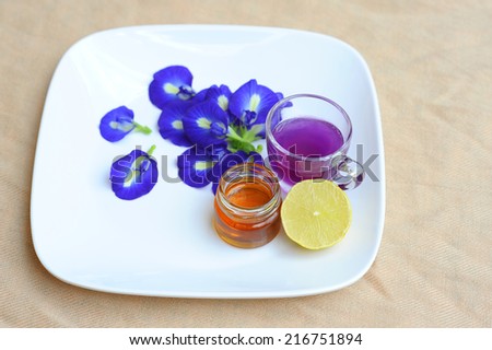 Butterfly Pea Juice in Glass, Lemon, Honey placed in a white dish on raw cotton background