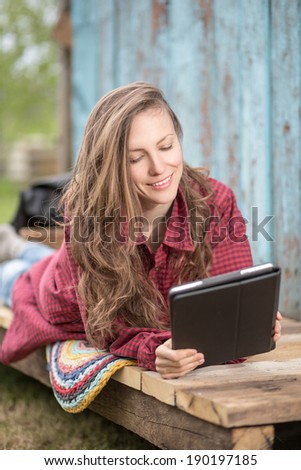 Happy young woman lying and holding digital tablet and smiling. soft daylight, focus on face
