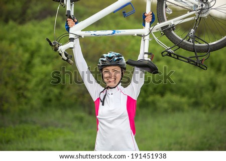 Young woman biker hold her bike up happy smiling outdoor. Cross country female biker relaxing after riding a bike