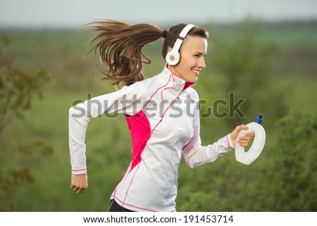 Running woman - female runner listening to music on smart phone hold water bottle outdoor in motion. Sporty beautiful woman jogging and listening to training music on smartphone