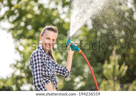 Summer garden, watering - beautiful woman watering lawn with garden hose in the garden. backlight