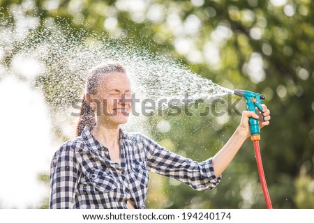 Beautiful young woman having fun in summer park, relaxing after work, watering lawn. Summer vacation concept. backlit