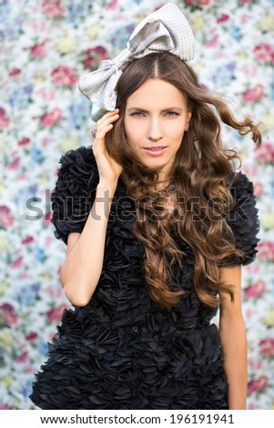 Portrait of a beautiful young brunette wearing black dress and bow hair accessory. studio shot