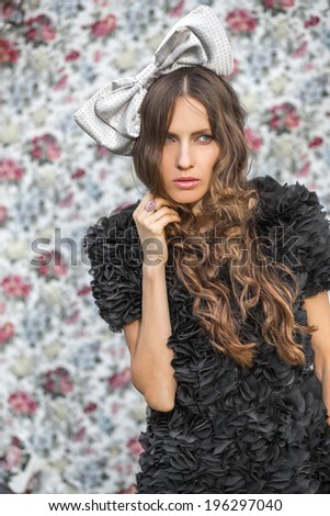 A portrait of a young woman with a grey bow in hair over flower background