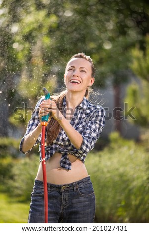 Beautiful young woman having fun in summer garden with garden hose splashing summer rain