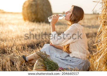 Portrait of young woman drink water bottle at summer sunny field. Sunshine, glow sun