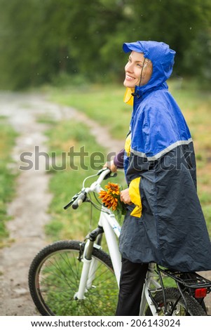 Beautiful smiling girl riding a bike in autumn rainy day