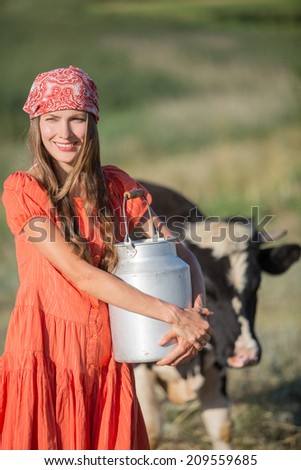 Female farmer is working on the organic farm with dairy cows and holding big milk container pot