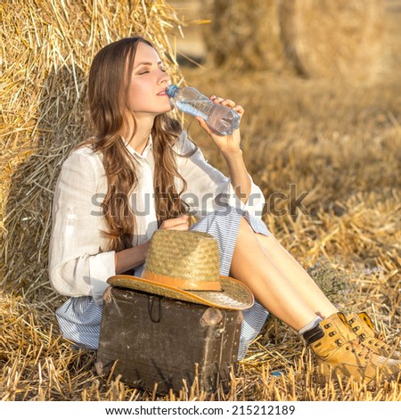 Attractive young traveler woman drinking water while sitting next to suitcase on a sunny day