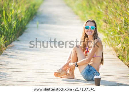 Beach vacation. Hot beautiful woman in bikini happy smiling sitting on bridge