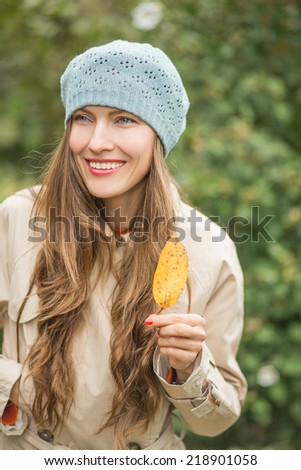 Beautiful autumn woman in autumn park holding autumn yellow leaf