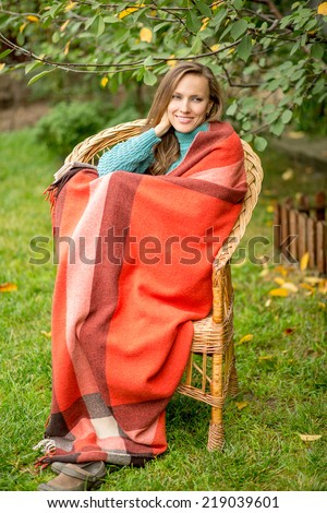 Beautiful woman in the garden wrapped in a plaid blanket sitting in armchair