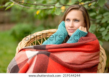 Beautiful woman in the garden wrapped in a plaid blanket sitting in armchair dreaming and planning her autumn vacation