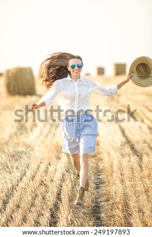 Young woman running on field in motion with outstretched arms, motion, soft daylight