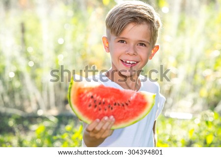 Funny kid eating watermelon outdoors in summer park, focus on face. Child, baby, healthy food