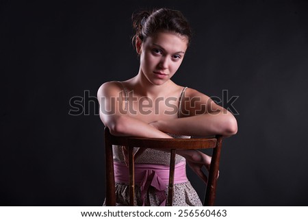 Horizontal portrait of a girl sitting on a chair on a black background, isolation
