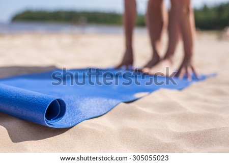 Girl doing yoga on a sunny day at the beach. Blue mat and blurred in the background hands and feet