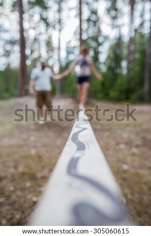 Learning to walk on a tightrope, and keep the balance. Man helping his girlfriend to keep balance
