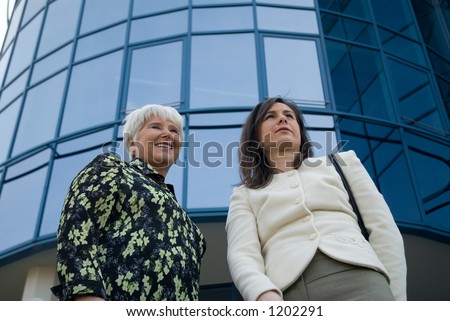 two women, elderly and young one discussing. Business building on background.  Low angle view